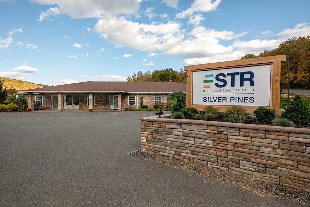 Exterior of STR Behavioral Health Silver Pines facility with signage, offering detox, addiction treatment, and mental health services.