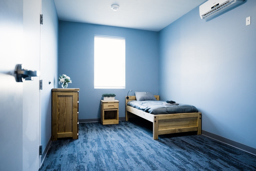 Private bedroom with single bed, dresser, and soft blue walls at Silver Pines detox and residential treatment center for addiction and mental health disorders.