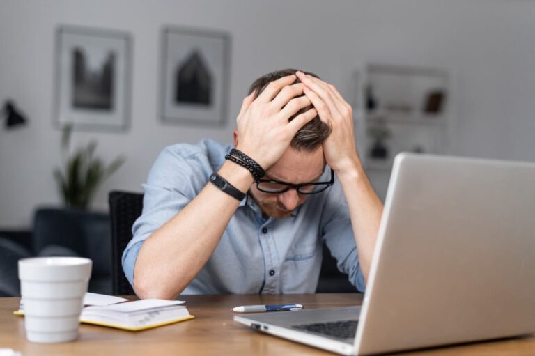 Man sits at his computer looking frustrated with his head in his hands.